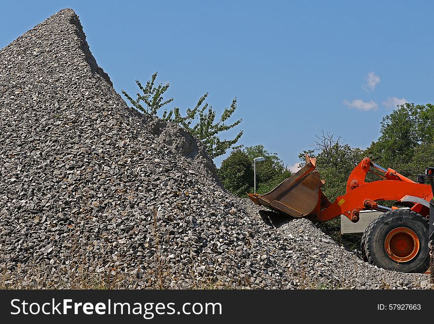 Excavator in front of a pile of rubble outside a mine against blue skies