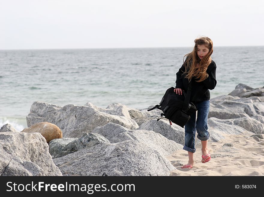 Young girl carrying her mothers camera bag across the beach. Young girl carrying her mothers camera bag across the beach