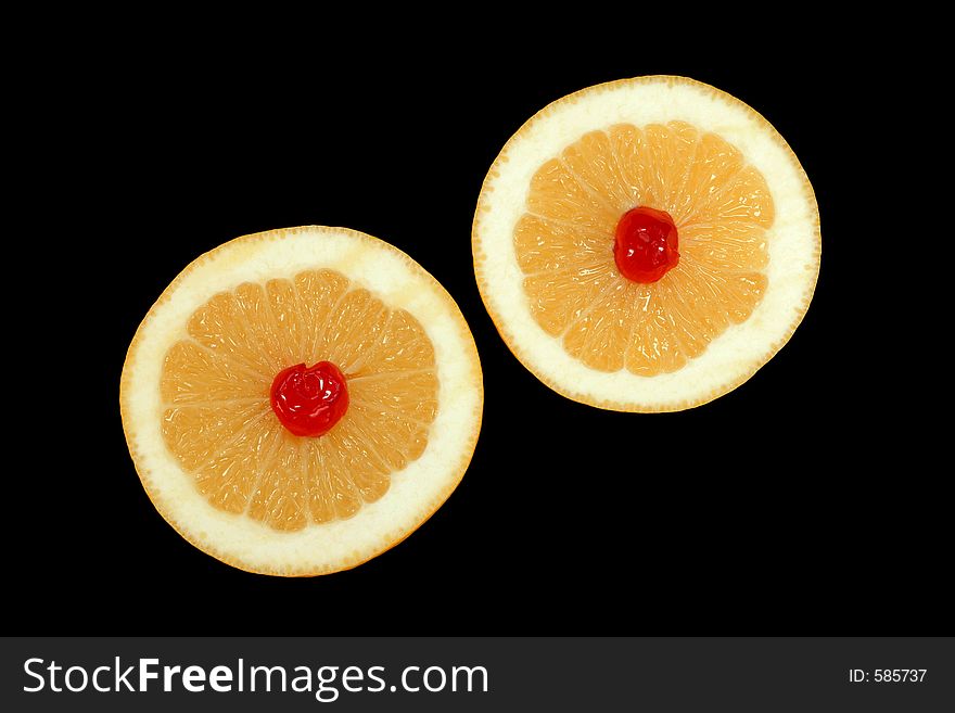 Two grapefruit halves with a red cherry at the centre of each, isolated on a black background. Two grapefruit halves with a red cherry at the centre of each, isolated on a black background.