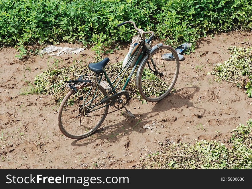 Old bicycle and a pair of blue plastic sandals parked in the dirt in the middle of a field. Old bicycle and a pair of blue plastic sandals parked in the dirt in the middle of a field