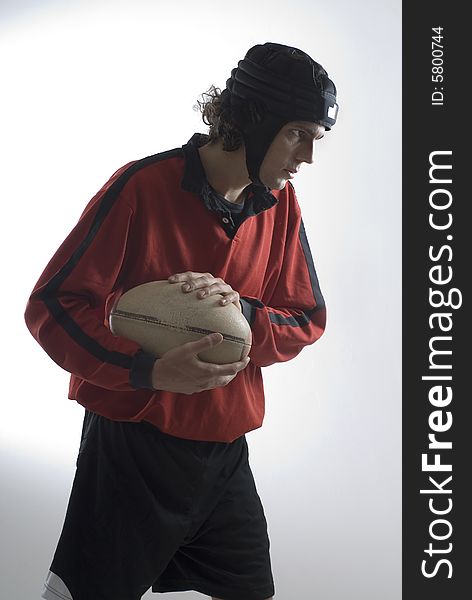 Man wearing a rugby helmet holds a rugby ball and has a serious look on his face. Vertically framed photograph. Man wearing a rugby helmet holds a rugby ball and has a serious look on his face. Vertically framed photograph