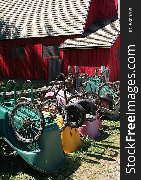 Colourful wheelbarrows lined up against a fence in front of a red barn
