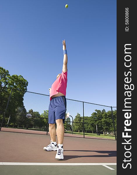A man is outside on a tennis court playing tennis.  He is reaching up to hit the ball and looking at his racket. A man is outside on a tennis court playing tennis.  He is reaching up to hit the ball and looking at his racket.