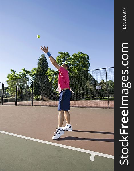 A man is outside on a tennis court playing tennis.  He is about to serve and looking at the ball in the air.  Vertically framed shot. A man is outside on a tennis court playing tennis.  He is about to serve and looking at the ball in the air.  Vertically framed shot.