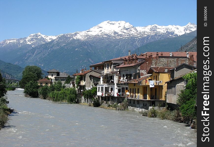 A small village alongside a river with the Italian Alps in the background in the Piedmont region. A small village alongside a river with the Italian Alps in the background in the Piedmont region