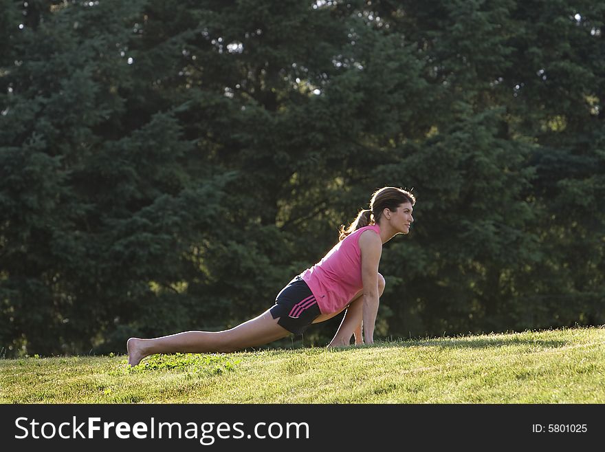 A woman doing stretches on a grassy lawn - Horizontally framed photograph. A woman doing stretches on a grassy lawn - Horizontally framed photograph