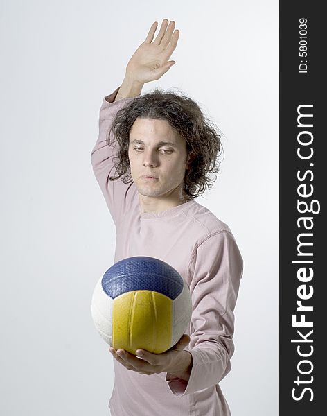 Man holds a volleyball in one hand and raises his other hand to serve it. Vertically framed photograph. Man holds a volleyball in one hand and raises his other hand to serve it. Vertically framed photograph