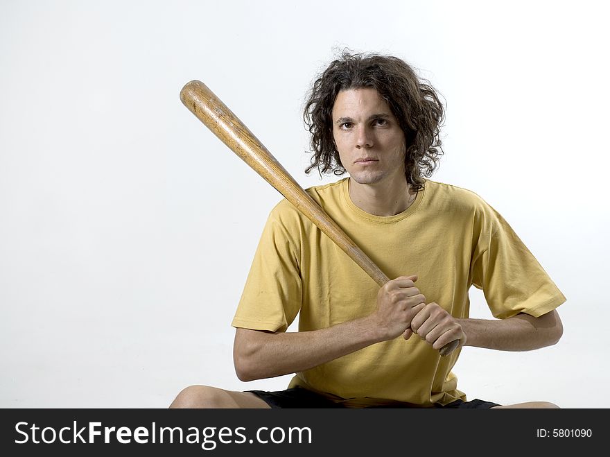 A man holding a baseball bat and sitting on the floor with a serious look on his face. Horizontally framed photograph. A man holding a baseball bat and sitting on the floor with a serious look on his face. Horizontally framed photograph