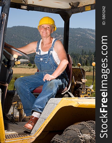 Senior woman on backhoe wearing yellow hardhat. Senior woman on backhoe wearing yellow hardhat