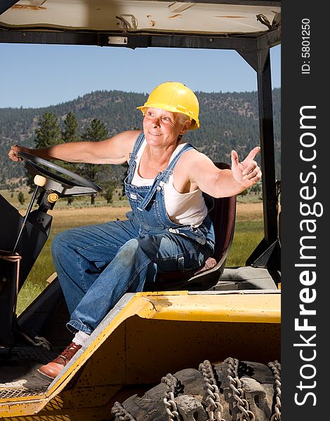 Senior woman on backhoe wearing yellow hardhat. Senior woman on backhoe wearing yellow hardhat