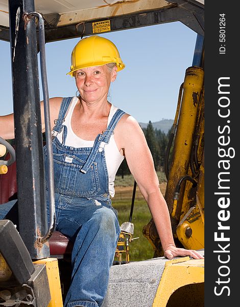 Senior woman on backhoe wearing yellow hardhat. Senior woman on backhoe wearing yellow hardhat