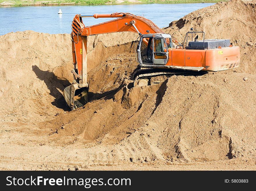 A photo of an excavator on the beach of the river.