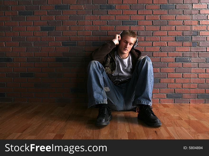 Grunge man in headphones next to brick wall and wood floor