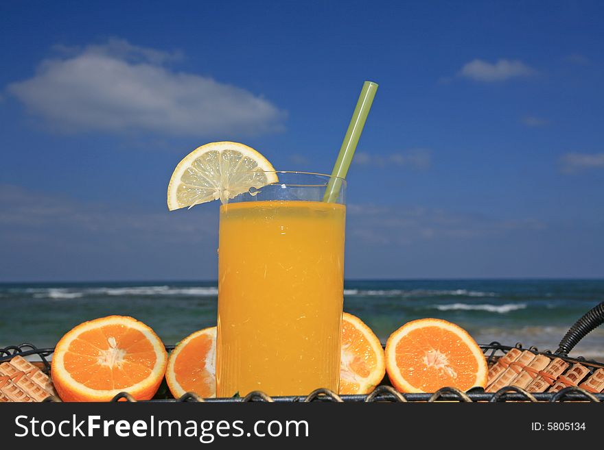 Glass of orange juice in surroundings fresh fruits on a background a sea-piece and blue sky