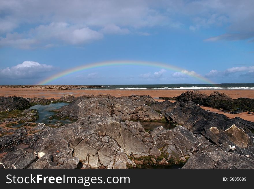 A rocky beach on a warm wet day with a calm sea and a rainbow after a shower an ideal place to have a walk in ireland. A rocky beach on a warm wet day with a calm sea and a rainbow after a shower an ideal place to have a walk in ireland