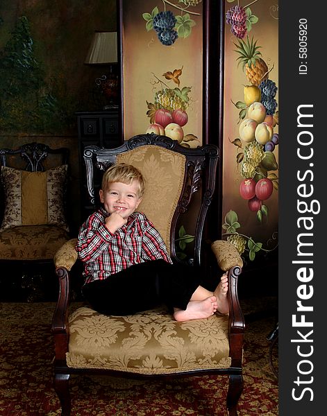 Boy sitting on an antique chair in red plaid shirt and black corduroy winter pants. Boy sitting on an antique chair in red plaid shirt and black corduroy winter pants