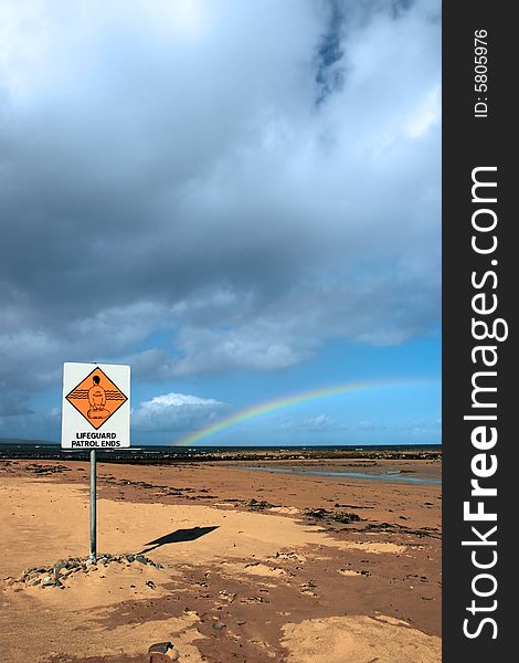 A sign warning that there is no lifeguard patrol beyond this sign with a beautiful rainbow in the background. A sign warning that there is no lifeguard patrol beyond this sign with a beautiful rainbow in the background