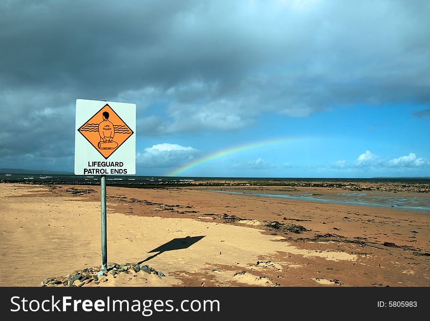 A sign warning that there is no lifeguard patrol beyond this sign with a beautiful rainbow in the background. A sign warning that there is no lifeguard patrol beyond this sign with a beautiful rainbow in the background