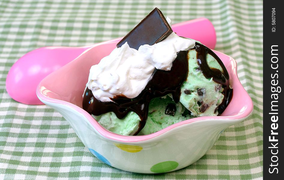 Mint candy tops a mint chocolate chip ice cream sundae in a pretty pink and green setting. Mint candy tops a mint chocolate chip ice cream sundae in a pretty pink and green setting.