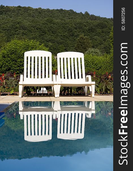 Two white sunloungers reflected in a blue swimming pool. Two white sunloungers reflected in a blue swimming pool