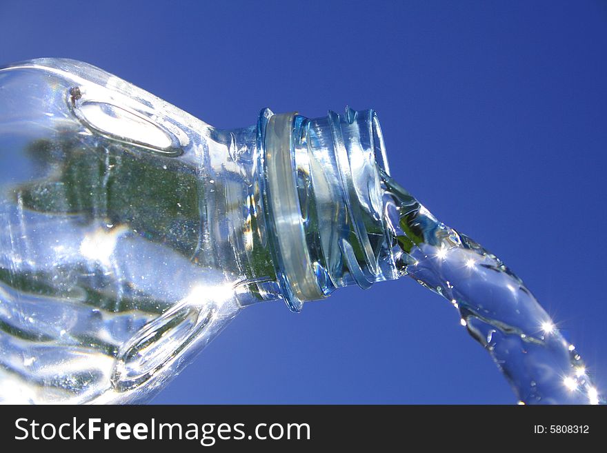 Beautiful clear water flows from a bottle against a blue sky. Beautiful clear water flows from a bottle against a blue sky