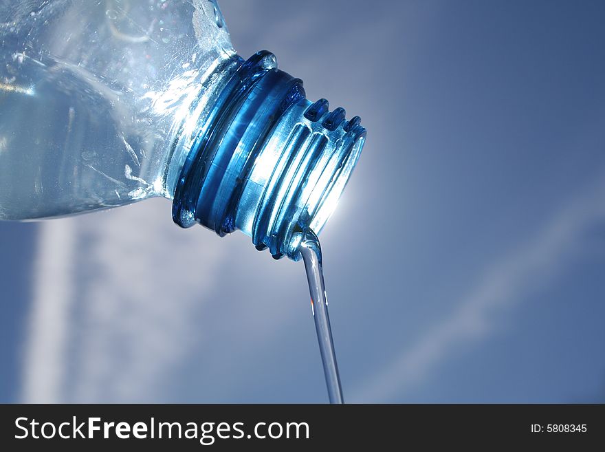 Beautiful clear water flows from a bottle against a blue sky sun. Beautiful clear water flows from a bottle against a blue sky sun