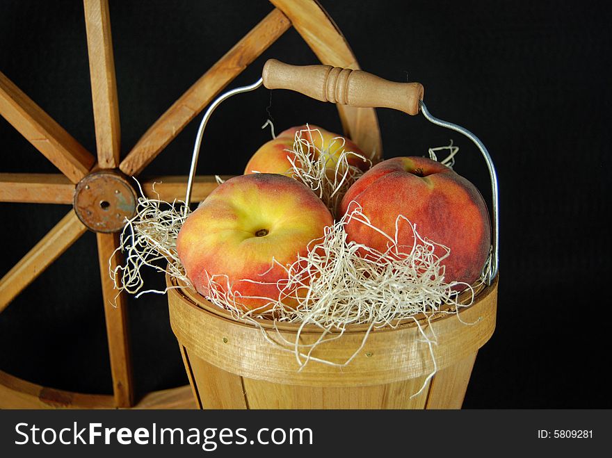 Peaches in a bushel basket with a wagon wheel. Peaches in a bushel basket with a wagon wheel.