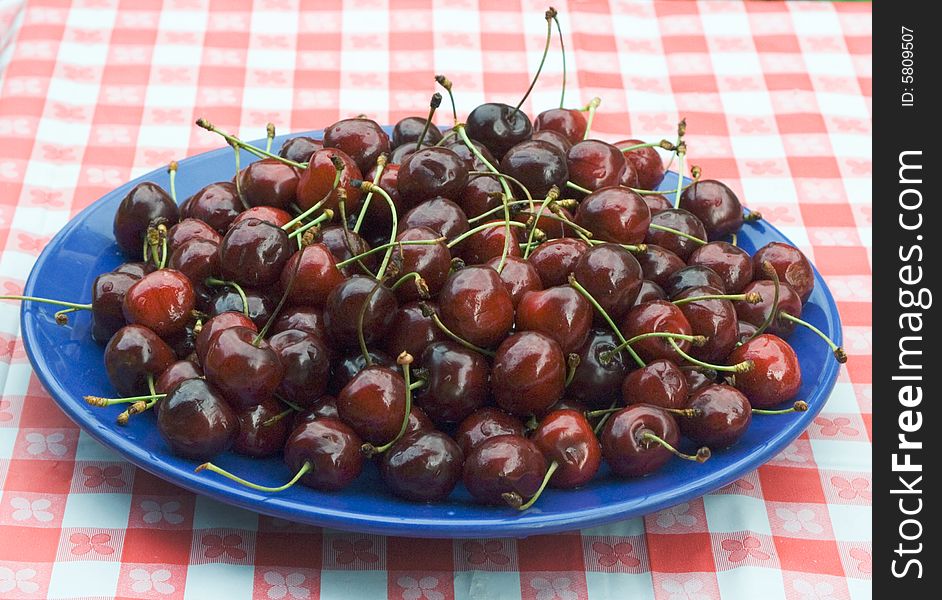 A plateful of sweet cherries on a table coverev with checkered buckram. A plateful of sweet cherries on a table coverev with checkered buckram