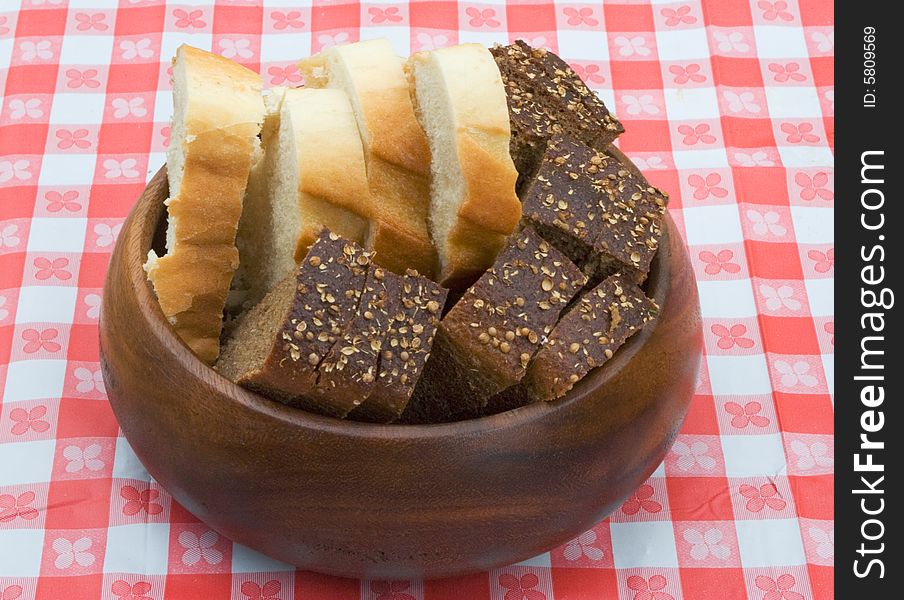 Slices of wheat and rye bread in a wooden bowl on a table covered with checkered buckram