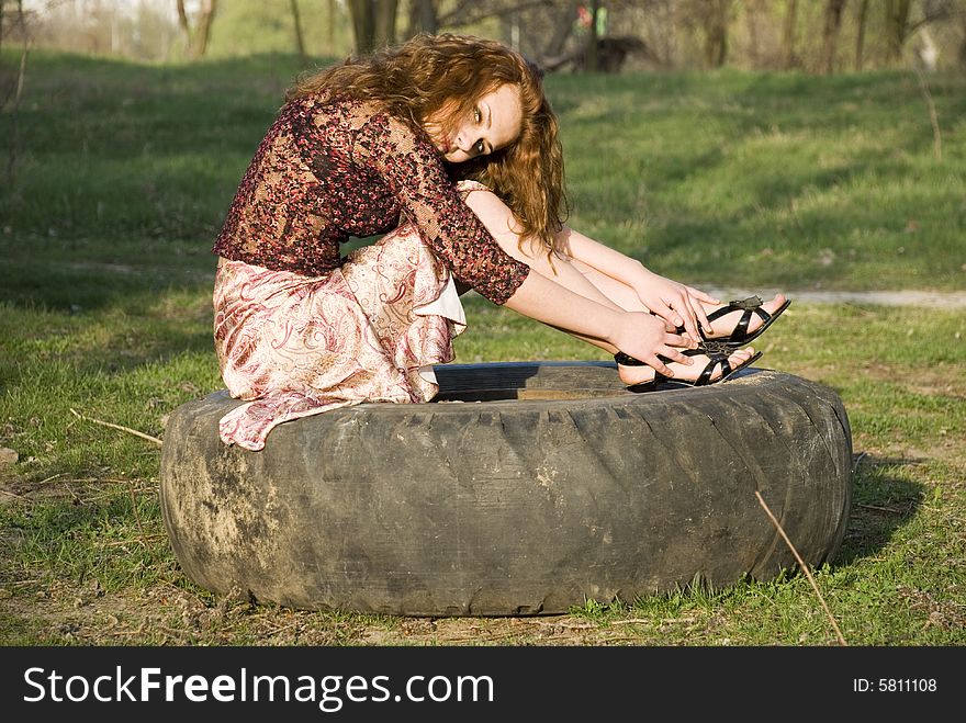 Portrait of young girl sitting on a motor-car tire in a park. Portrait of young girl sitting on a motor-car tire in a park