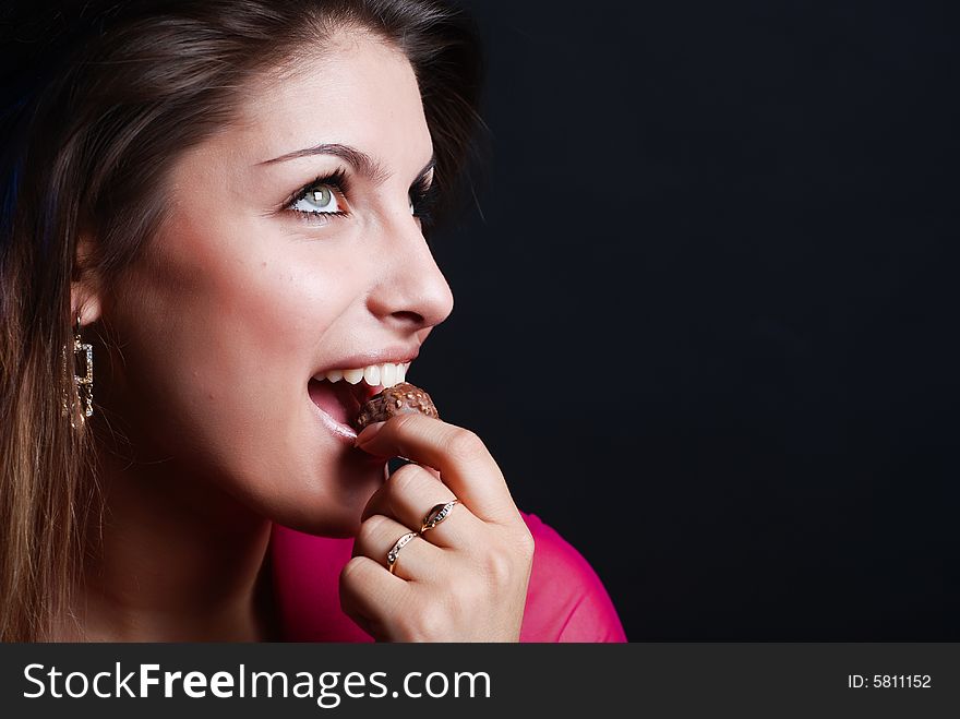 Portrait of beautiful girl in a pink woman's jacket with a chocolate candy in the mouth