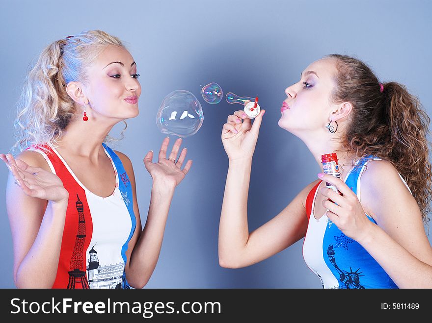 Two beautiful girls dressed in identical shirts play, inflating soap-bubbles. Two beautiful girls dressed in identical shirts play, inflating soap-bubbles