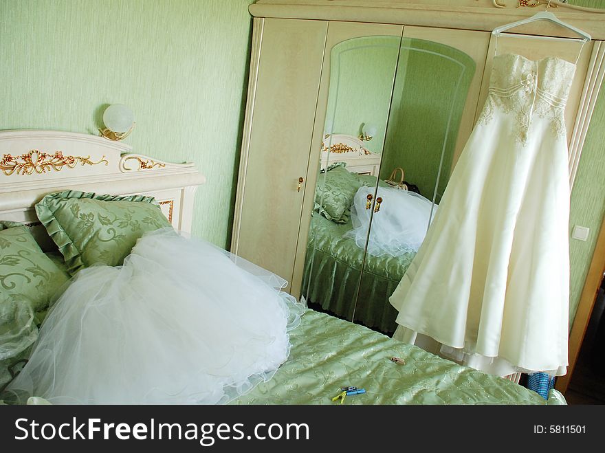A bedroom in which standing the closet of clothes and bed. A white bridal veil lies on a bed, a wedding-dress hangs on a closet. A bedroom in which standing the closet of clothes and bed. A white bridal veil lies on a bed, a wedding-dress hangs on a closet