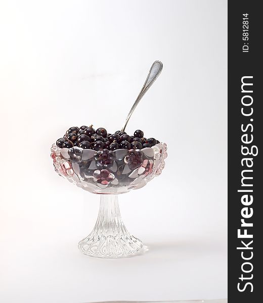 Berries of a black currant lay in a glass vase on a white backgroun