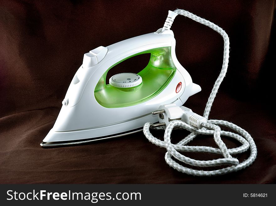 The electric iron stands on a brown background