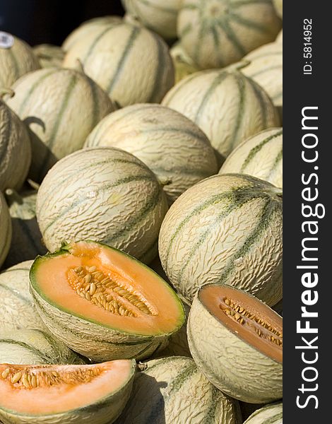 Several melons laid out at a market, some cut open