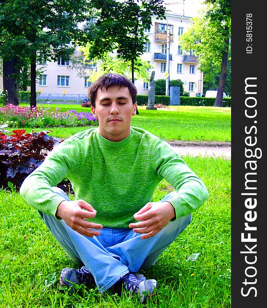 Photo of the young man meditating on a grass.