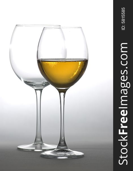 Two tall wine glasses on light background, one filled with white wine