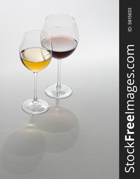 Two tall glasses on light background filled with red and white wine