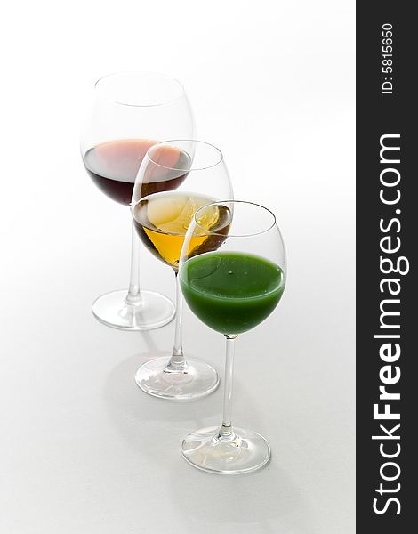 Three tall glasses on white background filled with: white, red wine and green cocktail