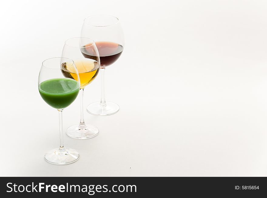 Three tall glasses on white background filled with: white, red wine and green cocktail