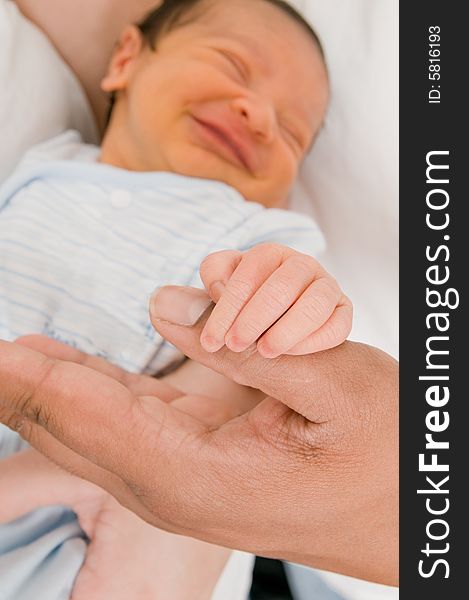 Baby's hand holding father's thumb with baby's grinning face in background. Baby's hand holding father's thumb with baby's grinning face in background