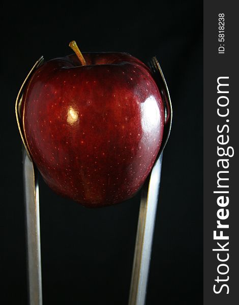 Kithcen tongs are holding an apple.