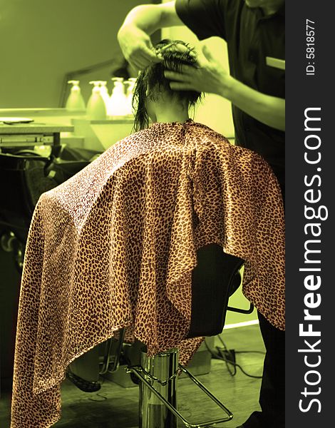 Girl seating in a salon chair with robe, getting a haircut; selective coloring