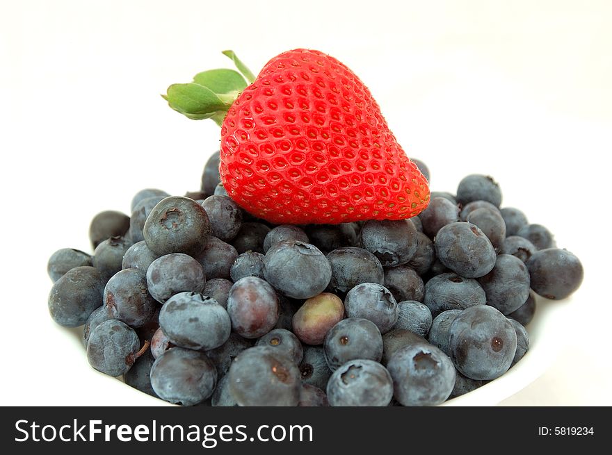 An image of a strawberry on top of a bowl full of fresh blueberries. An image of a strawberry on top of a bowl full of fresh blueberries.