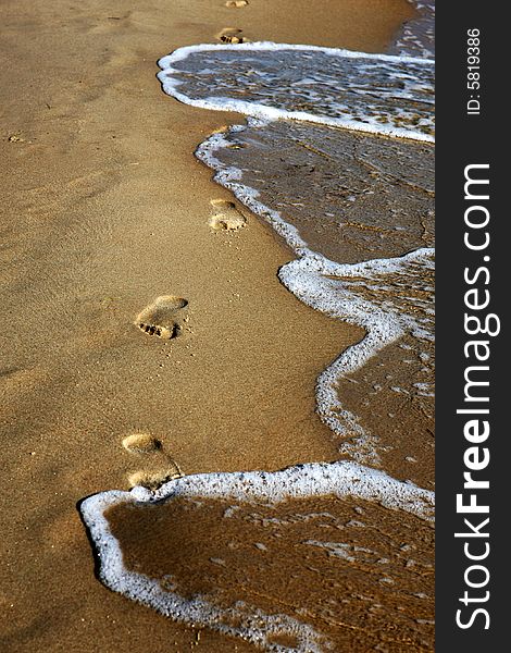 Footprints in the sand beeing washed away by a wave. Footprints in the sand beeing washed away by a wave