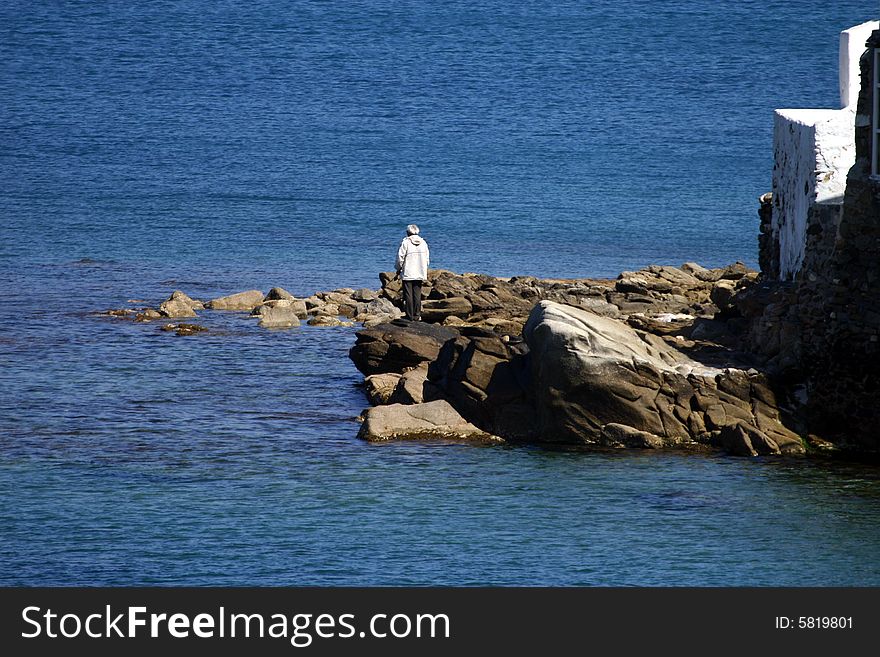 An elderly man standing on the rocks by the surf. An elderly man standing on the rocks by the surf.