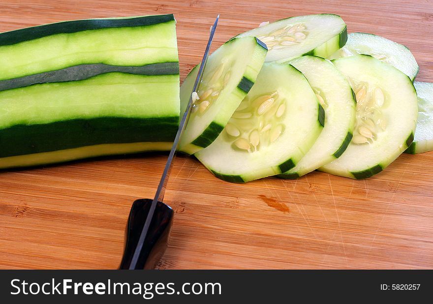 Cucumber on cutting board being decoratively sliced. Cucumber on cutting board being decoratively sliced.