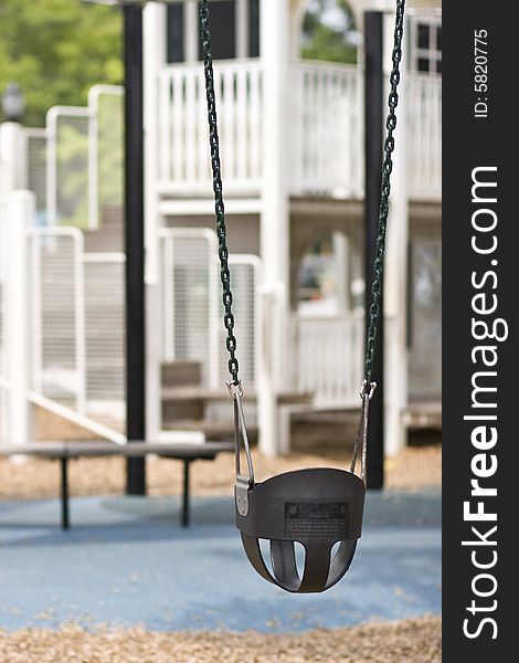 Infant swing on playground in foreground, play equipment out of focus in background