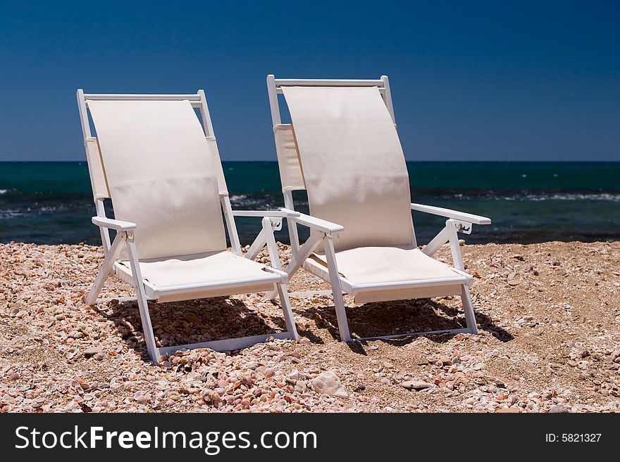 Two white chairs on a beach with sea shell and sand